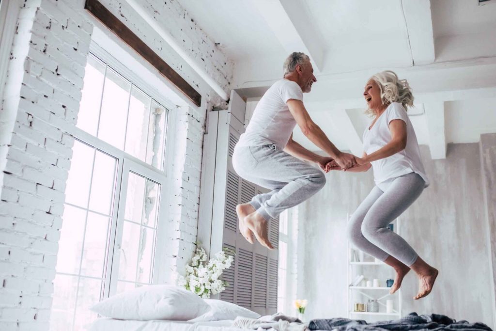 Happy senior couple bouncing on bed laughing together